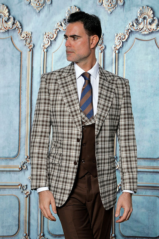 A man wearing the INSOMNIA PARIS-6 3-Piece Tailored Fit Plaid Formal Business Brown Suit by Insomnia stands before an ornate blue and white wall.