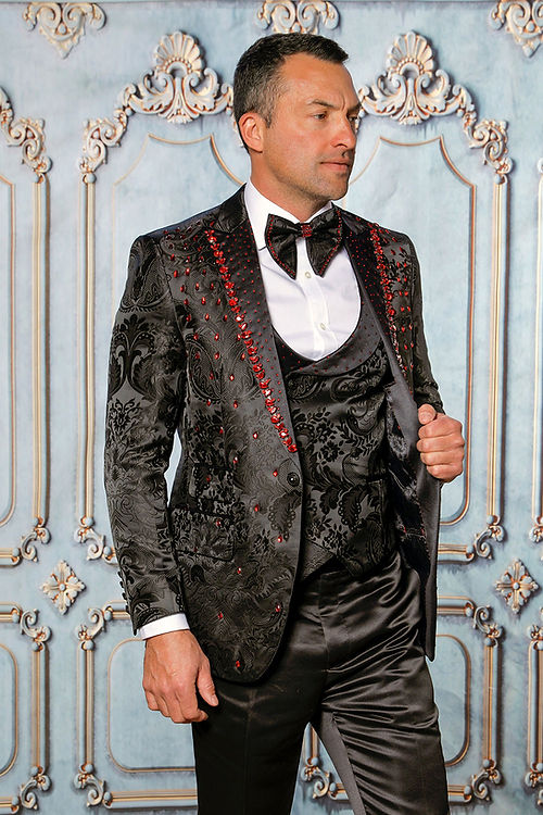 A man stands poised against an elegant, floral texture backdrop in a MANZINI PLATINUM 3-Piece Slim Fit Rhinestone Satin Floral Black/Red Tuxedo Suit by Insomnia.