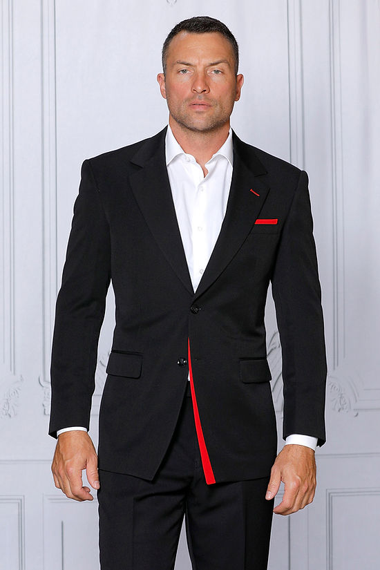 A man faces forward wearing the MANZINI PURPLE LABEL 2-Piece Tailored-Fit Men's 4-Way Stretch Spandex Suit in Black/Red by Manzini, featuring a white dress shirt, red pocket square, and red jacket trim.