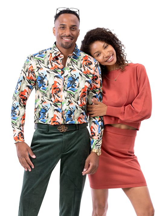 A man wearing an EJ SAMUEL floral shirt paired with EJ Samuel Hunter Pants PV01 smiles beside a woman in a rust-colored outfit, who leans on his shoulder as they both strike a friendly pose.