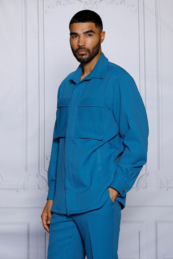 A man wearing the Insomnia INSOMNIA ROBERTO 2PC Teal Leisure Suit stands in front of an ornate white wall.