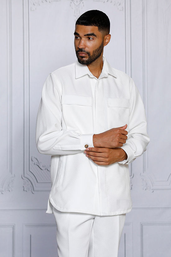 A man with short hair and a beard wears the INSOMNIA ROBERTO 2PC White Leisure Suit by Insomnia, standing against an ornate light-colored wall.