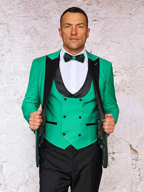 A man in an Insomnia MANZINI ROME Slim Fit 3-Piece Stretch Spandex Apple Green Tuxedo Suit with black lapels and a matching bow tie stands against a textured wall.