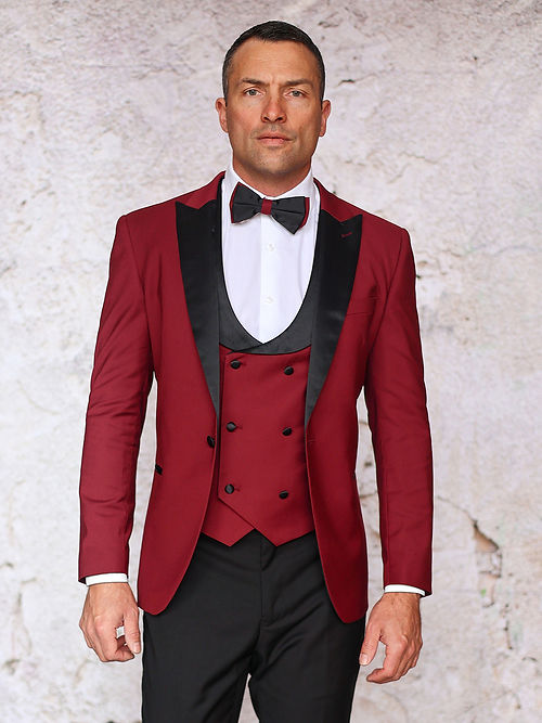 A person in an Insomnia MANZINI ROME Slim Fit 3-Piece Stretch Spandex Burgundy Tuxedo Suit with black lapels, a classic black bow tie, and a crisp white shirt stands against a textured light background.