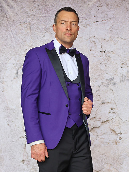 A man in an Insomnia MANZINI ROME Slim Fit 3-Piece Stretch Spandex Purple Tuxedo Suit with a black lapel, white shirt, and black bow tie stands against a textured light background.
