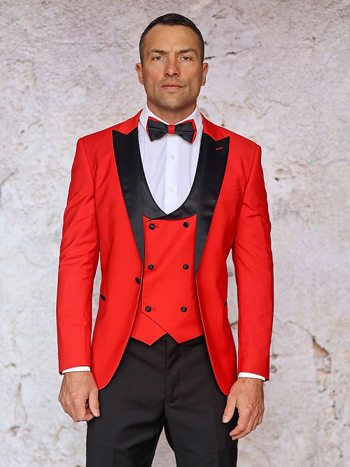 A man stands against a textured wall, highlighting the sleekness of the MANZINI ROME Slim Fit 3-Piece Stretch Spandex Red Tuxedo Suit by Insomnia, featuring a black lapel and bow tie.