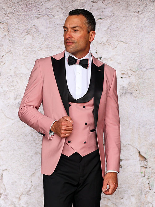 A man in a MANZINI ROME Slim Fit 3-Piece Stretch Spandex Rose Gold Tuxedo Suit by Insomnia, featuring black lapels and a bow tie, stands sideways against a textured wall. Dry clean only.