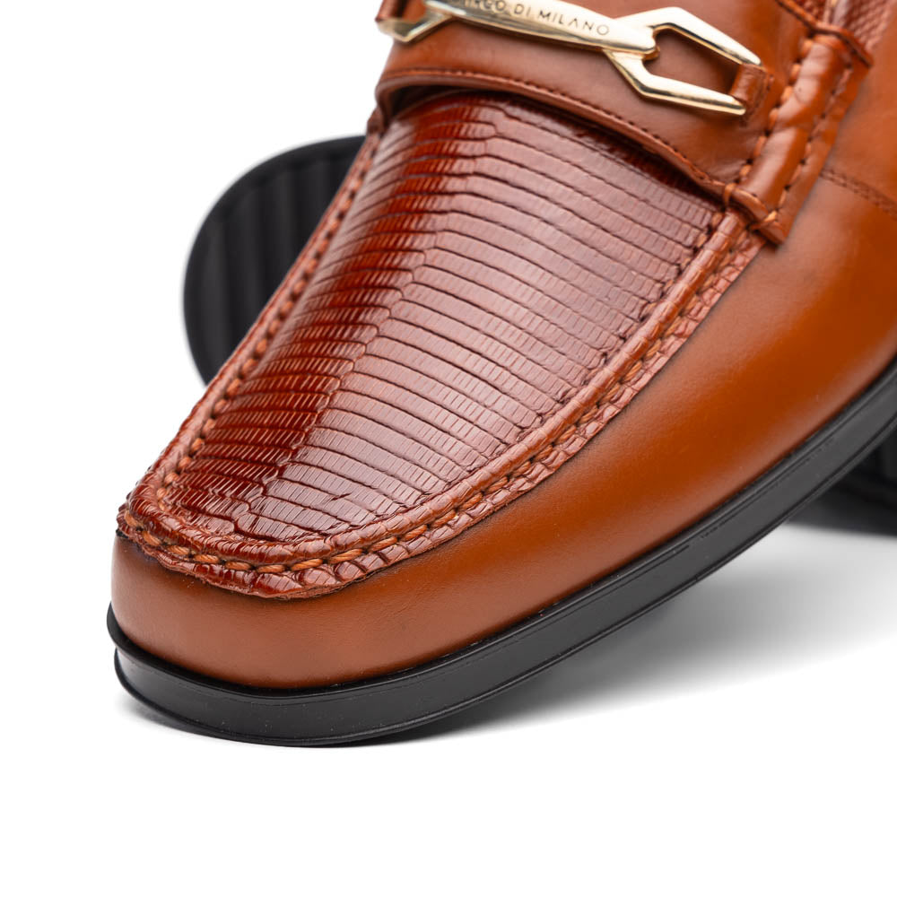 The Marco Di Milano Ravello Cognac loafers feature brown leather with hand-painted finishes and metal detailing; one shoe is upright, while the other displays the black ridged sole.