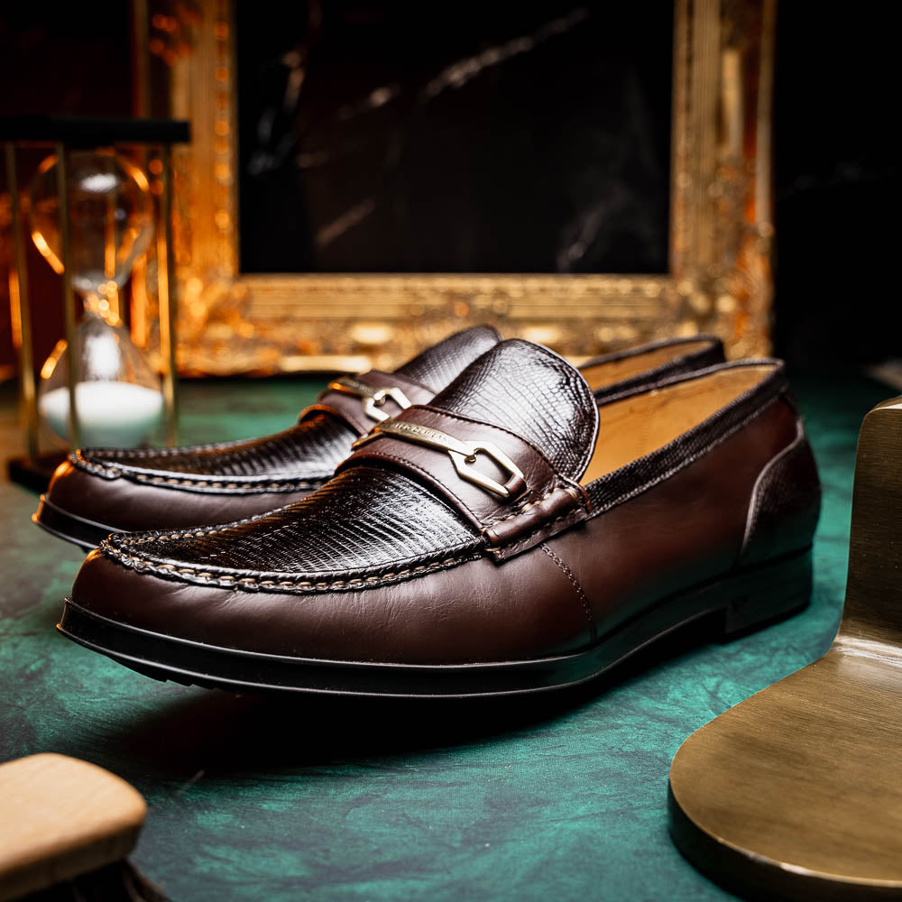 The Marco Di Milano Ravello Brown loafers, crafted from genuine lizard with a metal buckle, are showcased with one shoe upright and the other on its side to highlight the elegant hand-painted finish.
