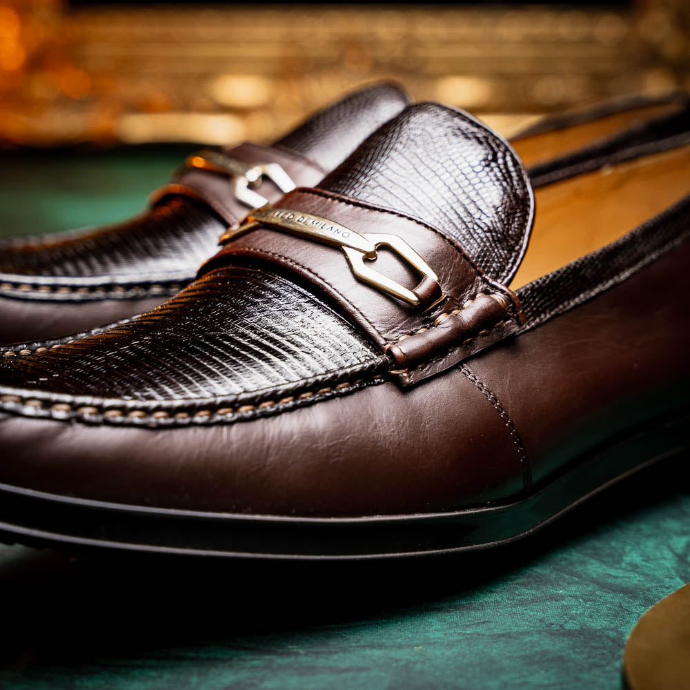 The Marco Di Milano Ravello Brown loafers, crafted from genuine lizard with a metal buckle, are showcased with one shoe upright and the other on its side to highlight the elegant hand-painted finish.
