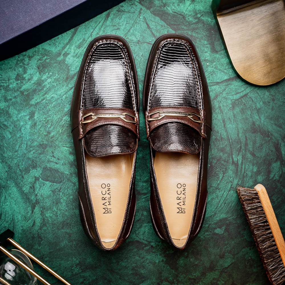 The Marco Di Milano Ravello Brown loafers, crafted from genuine lizard with a metal buckle, are showcased with one shoe upright and the other on its side to highlight the elegant hand-painted finish.
