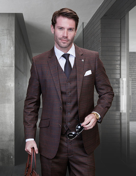 A man in a modern fit STATEMENT CLOTHING | SANTORI-COPPER suit by Statement Clothing, with a white shirt and dark tie, stands indoors holding sunglasses and a leather bag, wearing a neutral expression.