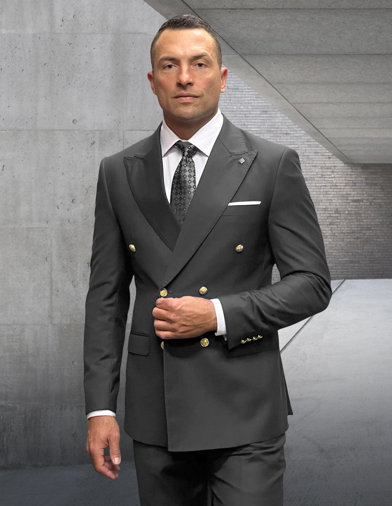A man in Statement Clothing's STATEMENT CLOTHING | SD-100-H.CHARCOAL tailored fit double-breasted suit with gold buttons, paired with a white shirt and patterned tie, stands in a modern concrete hallway.