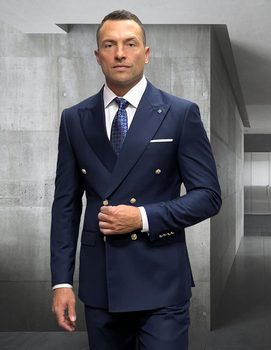 A man in the STATEMENT CLOTHING | SD-100-NAVY tailored navy suit by Statement Clothing, featuring gold buttons, stands indoors against a gray concrete wall background.