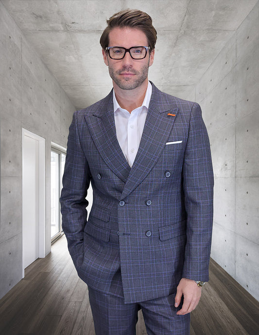 A man wearing the STATEMENT CLOTHING | SD-102-CHARCOAL double-breasted suit by Statement Clothing stands in a modern hallway with concrete walls and wooden flooring, paired with tailored fit pants and glasses.