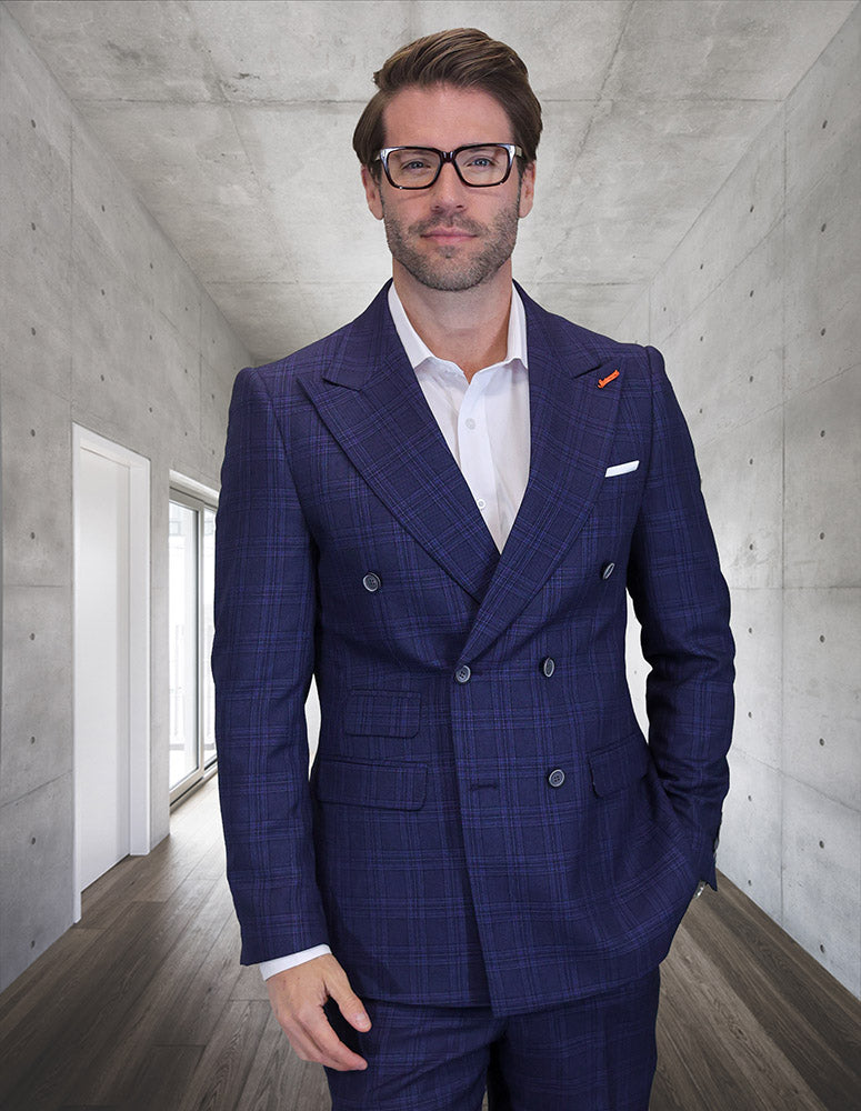 A man in STATEMENT CLOTHING | SD-102-SAPPHIRE by Statement Clothing and glasses stands in a sleek hallway with concrete walls and wooden flooring, looking at the camera.