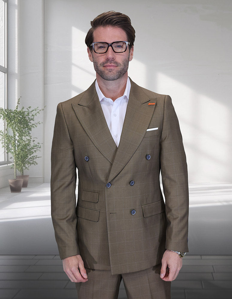 A man in the STATEMENT CLOTHING | SD-104-BRONZE double-breasted suit by Statement Clothing and a white shirt stands indoors near a sunlit window with a potted plant in the background.