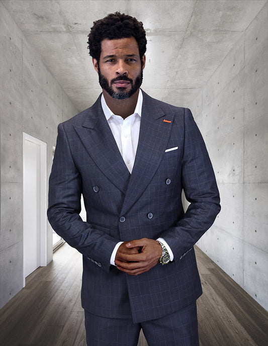 A bearded man wearing the STATEMENT CLOTHING | SD-104-CHARCOAL modern fit suit by Statement Clothing stands in a minimalist hallway with concrete walls and wood flooring.