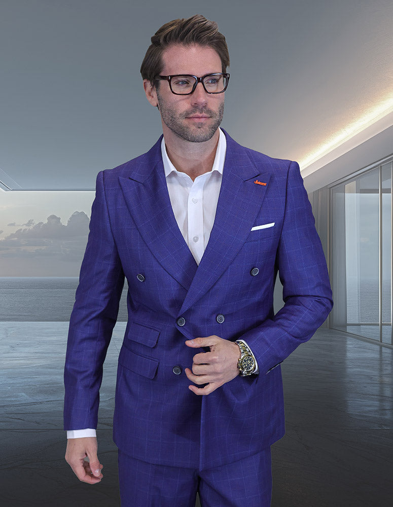 A man in glasses wears the STATEMENT CLOTHING | SD-104-INDIGO, a modern fit indigo double-breasted suit by Statement Clothing, with a white shirt. He stands indoors by large windows overlooking an ocean view.