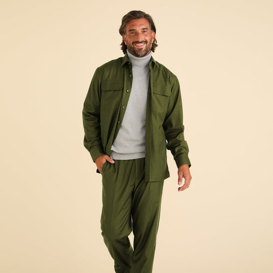 A man stands against a beige background wearing Inserch Modern Fit Pants P3199S-20 Chive, paired with a green button-up shirt and a light gray turtleneck sweater.