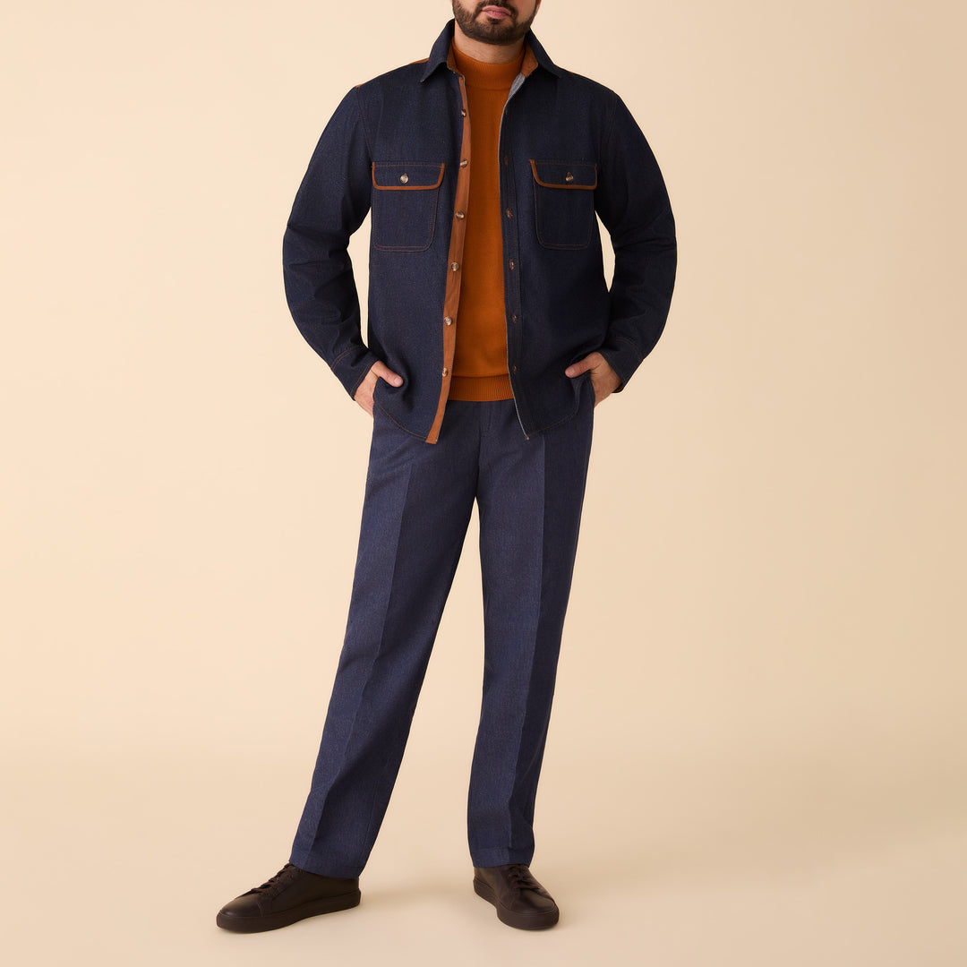 A man stands against a beige background wearing the Inserch Denim Shirt w/ Suede Trim 2pc Set in indigo by Inserch, paired with an orange sweater and dark brown shoes.