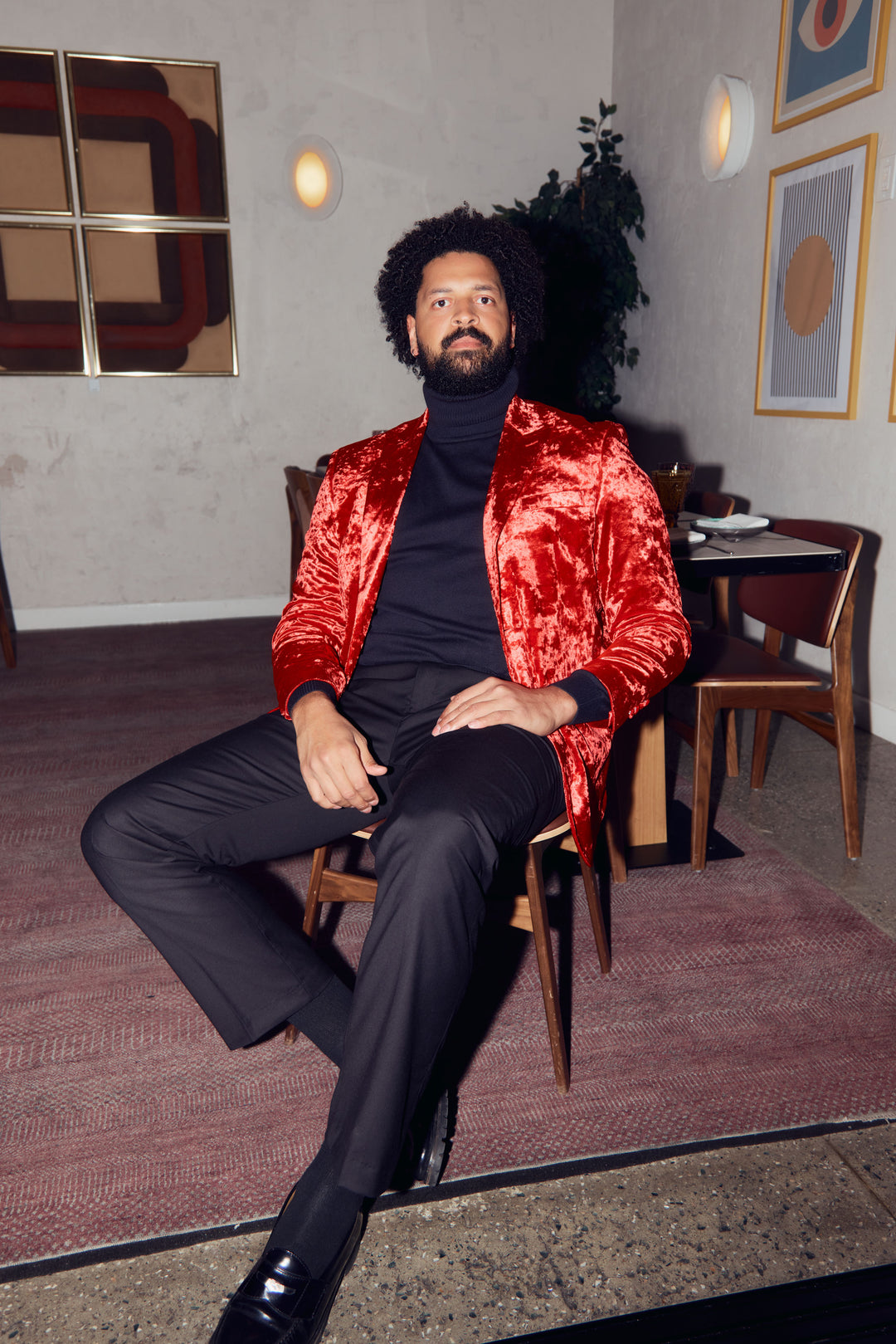 A man wearing the Inserch Crushed Velvet Blazer BL008-00030 Red by Inserch over a black turtleneck and black pants stands against a beige background.