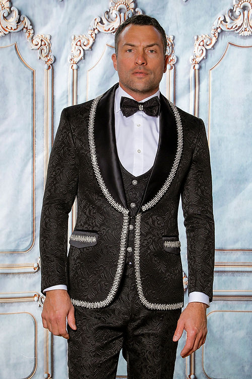 A man in an Insomnia MANZINI SOFIA 3-Piece shiny rhinestone trim floral textured black/silver tuxedo stands against a decorative backdrop.