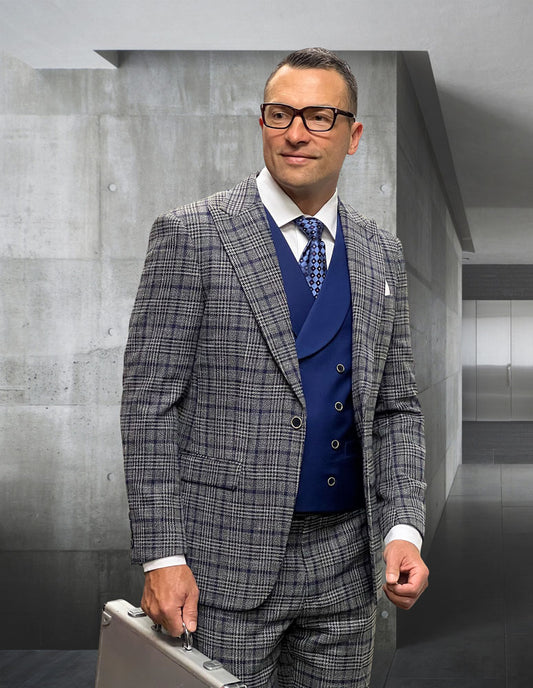 A man in the STATEMENT CLOTHING | SORENTO-GRAY suit by Statement Clothing, with a blue vest, white shirt, and patterned tie, holds a silver briefcase in a sleek gray concrete hallway.