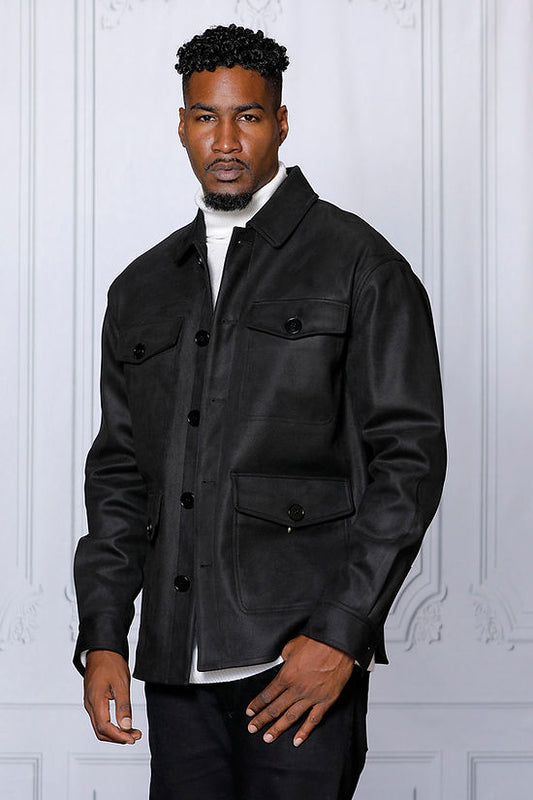 A man in a MANZINI SPAIN black large pockets button-up winter coat by Insomnia, made from refined poly blend fabric, stands over a white turtleneck against a white-paneled wall.