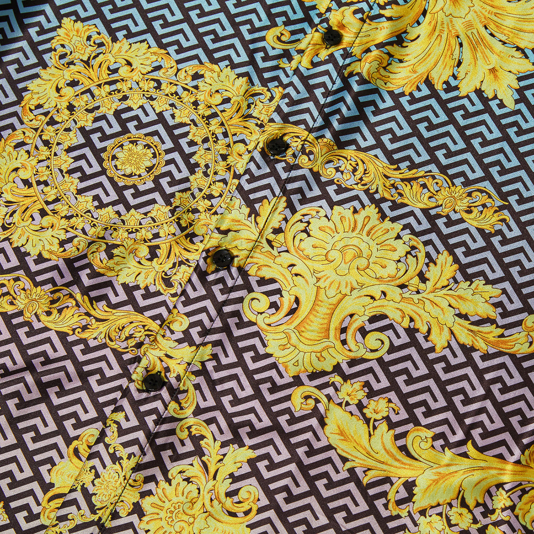 A man wears the Inserch SS Grecian Print Shirt SS053-00066 Multi—a short-sleeve shirt with bold geometric and baroque yellow patterns—standing against a plain beige background.