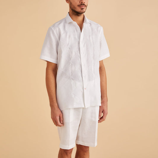 An individual wearing the Inserch SS Linen Embroidered Shirt, a white, short-sleeved design by Inserch, paired with shorts stands against a beige background.