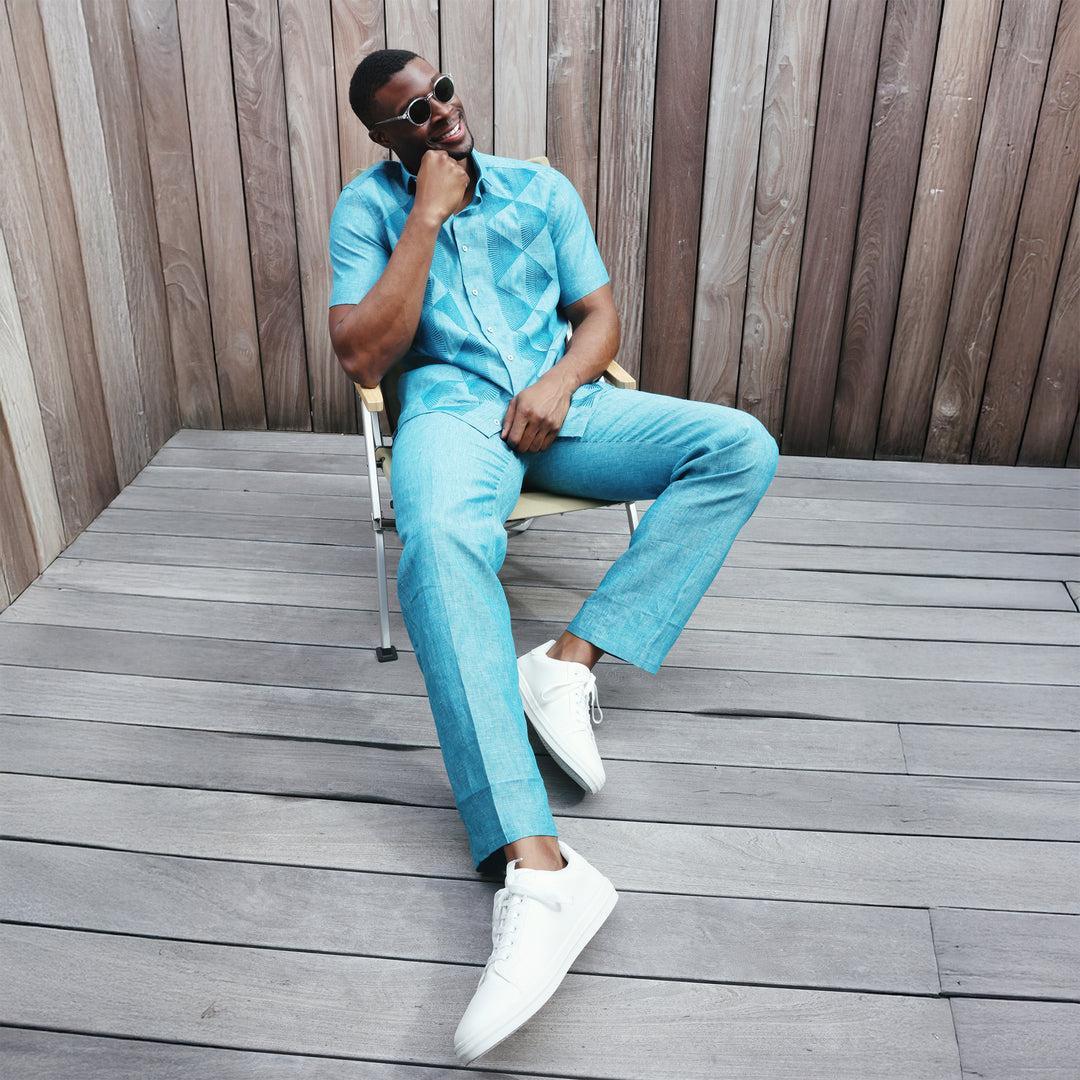 A man in an Inserch SS Linen Embroidered Shirt SS126-00172 Caspian, a teal short-sleeve button-up made from premium European linen, paired with matching geometric pants, stands against a plain beige background.