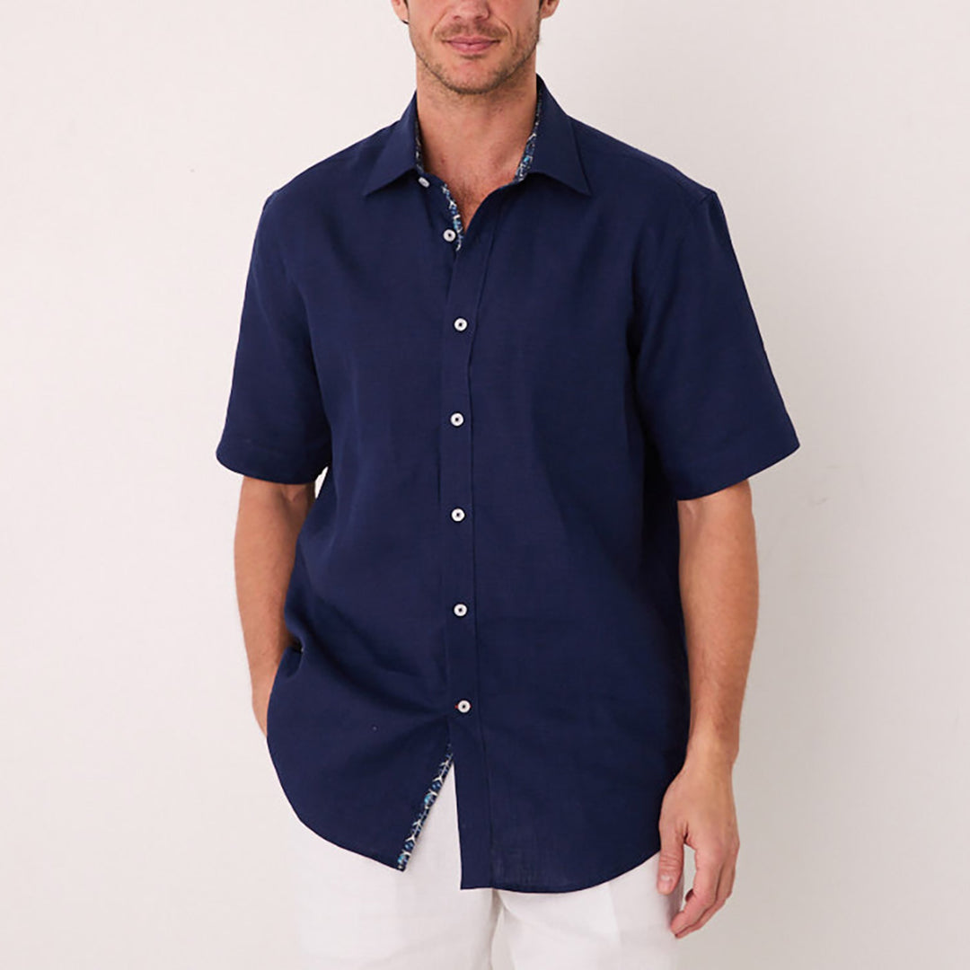 A person wearing an Inserch SS Linen Shirt in Ink stands against a plain light-colored background. The short-sleeve shirt features a contrasting floral print on the inner collar and placket, adding unexpected contrast.