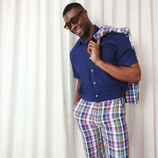 Man wearing the Inserch Linen 2pc Set (Shirts and Pants) (SS717) in Ink by Inserch, styled with sunglasses and a matching plaid jacket over his shoulder, stands in front of a white curtain.
