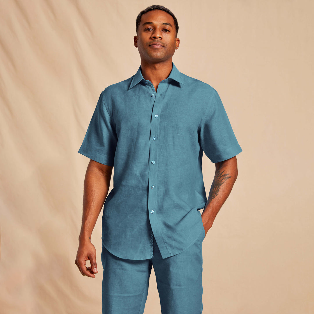 A man stands against a beige backdrop wearing the Inserch Linen 2pc Set (Shirts and Pants) SS717 in Caspian blue by Inserch, with one hand in his pocket.