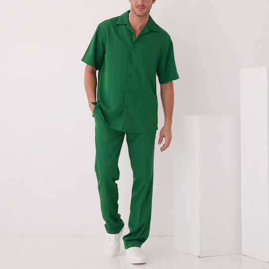 A man wears the Inserch Crepe Camp Collar Shirt SS9356-00200 in emerald and matching pants, standing indoors against a plain white background with one hand in his pocket and white sneakers on.