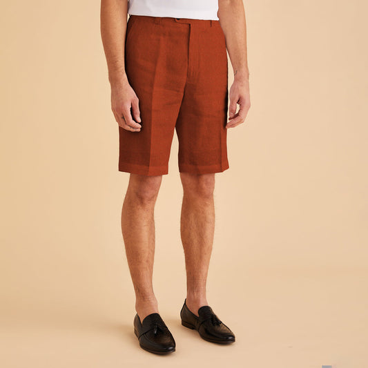 A man stands against a beige background wearing Inserch Modern Linen Shorts ST31-00109 in Burnt Orange and black loafers.