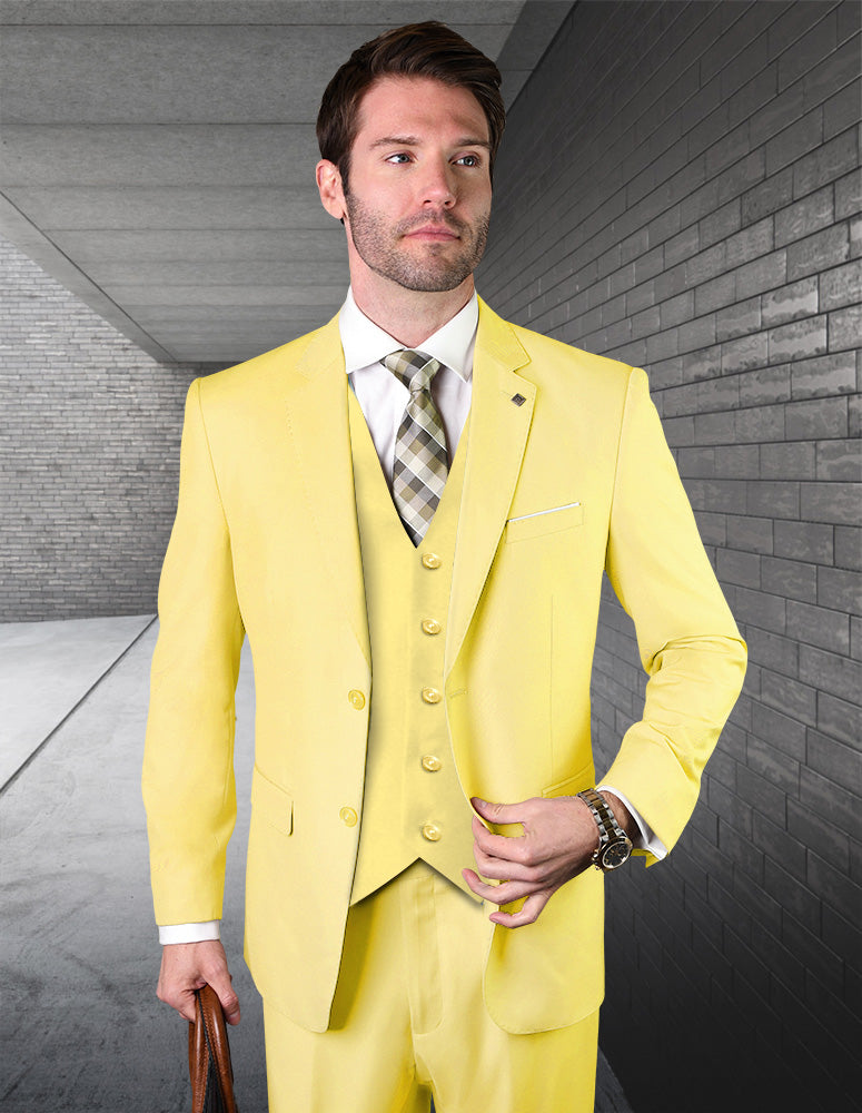 A man in the STATEMENT CLOTHING | STZV-102-YELLOW modern fit Italian wool suit by Statement Clothing, with a white shirt and plaid tie, stands on a sleek gray urban walkway holding a brown bag.