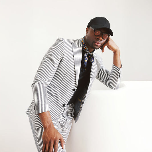 A man dons the Inserch Seersucker Stripe Blazer SU660155-00001 Black, paired with a white shirt, standing against a beige background.