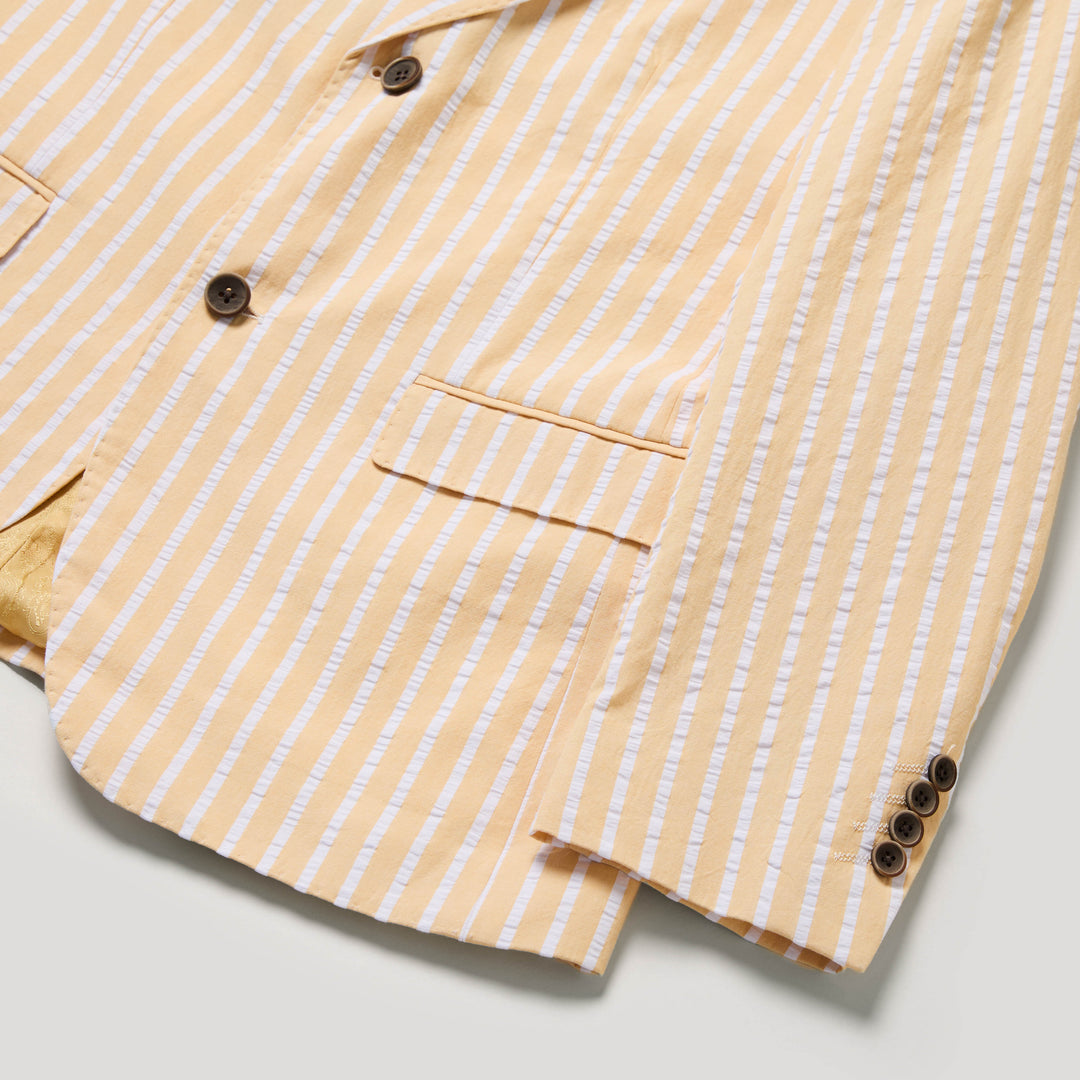 Close-up of the Inserch Wide Stripe Seersucker Suit Long SU660507L-00055 Yuzu blazer by Inserch, featuring yellow and white stripes, brown buttons, and flap pockets, laid flat on a light surface.