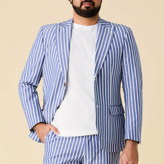 A man wears the Inserch Wide Stripe Seersucker Suit Long SU660507L-00181 in River Blue by Inserch, paired with a plain white t-shirt, standing against a beige background.