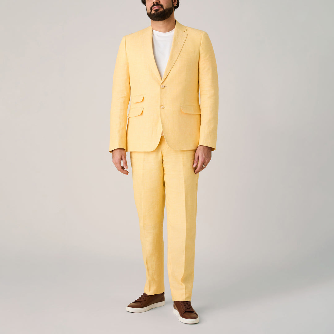 A man wearing the Inserch Slim Linen Blazer SU880-00055 Yuzu by Inserch, paired with a white t-shirt and brown sneakers, stands against a plain light background.