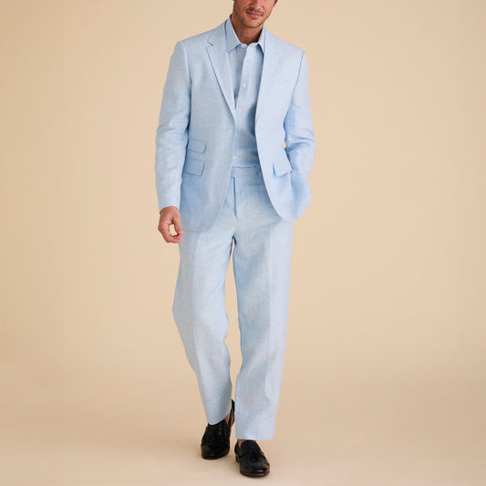 Showcasing the Inserch Slim Linen Suit SU880-00183 in Blue Mist, a person stands poised against a beige background, pairing the serene set with matching shirts and sleek black shoes. This ensemble underscores the sophisticated texture of its yarn-dye fabric.