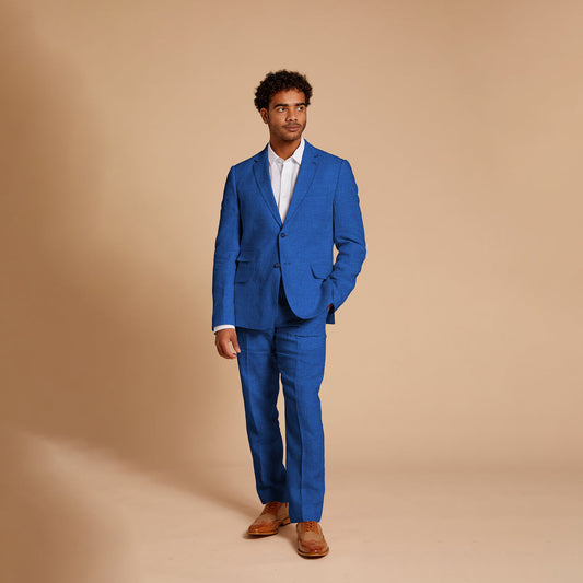 A man in an Inserch Slim Linen Suit SU880-00181 River Blue paired with a crisp white shirt stands against a plain beige background, gazing to the side.