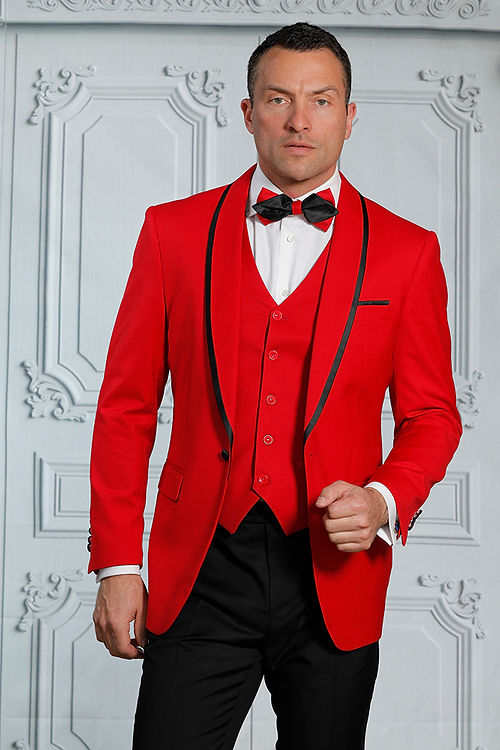A man stands confidently against an ornate white background, wearing the MANZINI SUNSET Slim Fit Red Tuxedo Suit by Insomnia. He sports a black bow tie and showcases the reversible vest made from breathable fabric.