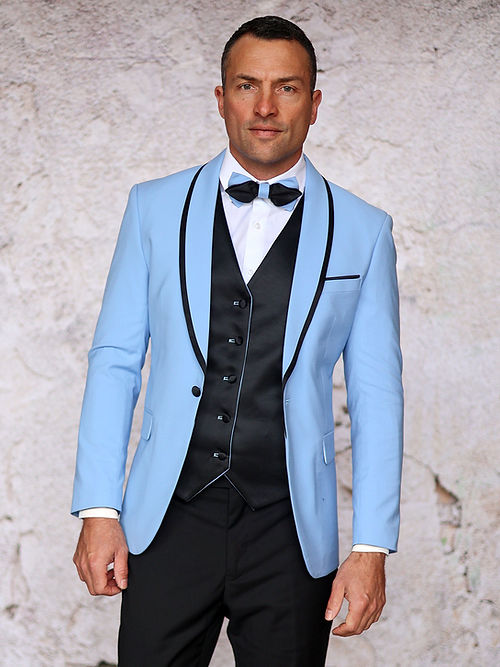 A man in an Insomnia MANZINI SUNSET Slim Fit 3-Piece Sky Black Tuxedo Suit with a reversible vest and bow tie stands against a textured wall.