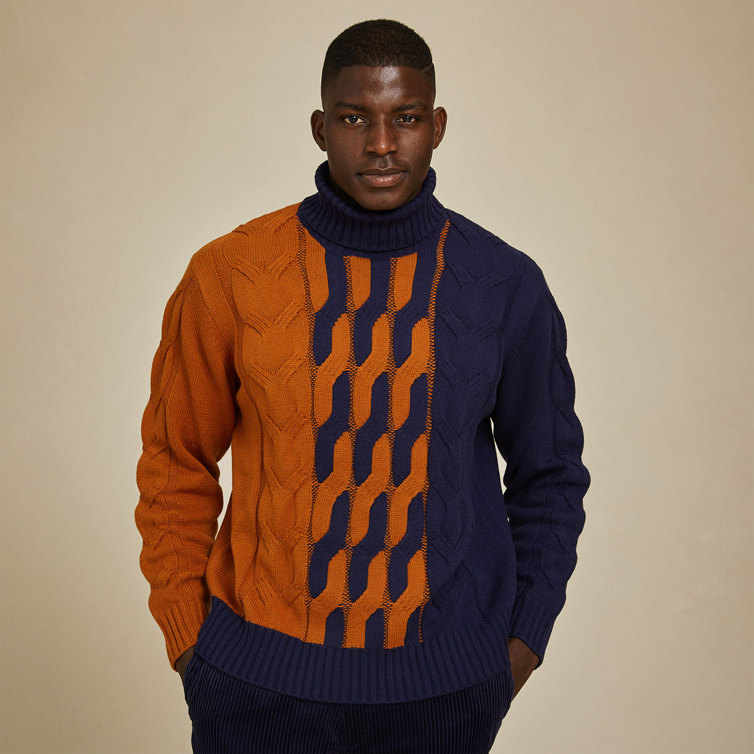 A man faces the camera, hands in pockets, wearing the Inserch Cotton Blend Cable Knit Turtleneck Sweater SW303-11 in navy by Inserch, featuring a colorblock design with orange and navy blue patterns.
