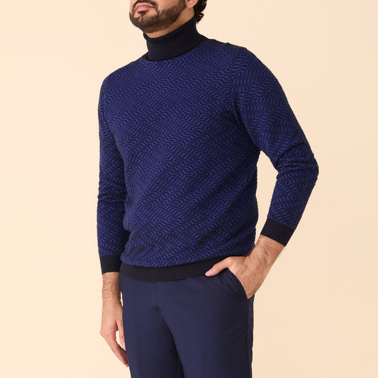 A man wearing the Inserch Intarsia Turtleneck Sweater SW304-00036 Ink by Inserch and dark blue pants stands against a plain beige background.