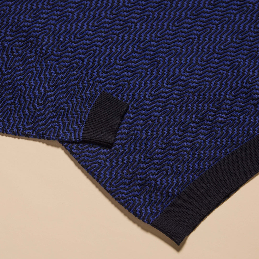 A man wearing the Inserch Intarsia Turtleneck Sweater SW304-00036 Ink by Inserch and dark blue pants stands against a plain beige background.