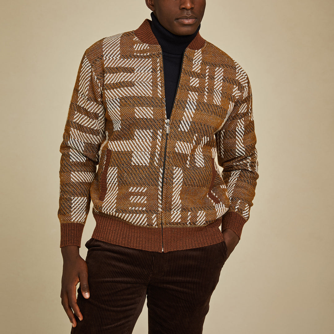 A man wears the Inserch Geometric Full Zip Baseball Knit Jacket SW609-27 Aztec over a black turtleneck and brown corduroy pants, standing against a plain beige background.